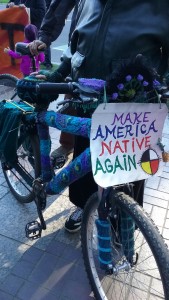 A bike covered in knitting bearing a sign that says "Make America native again."