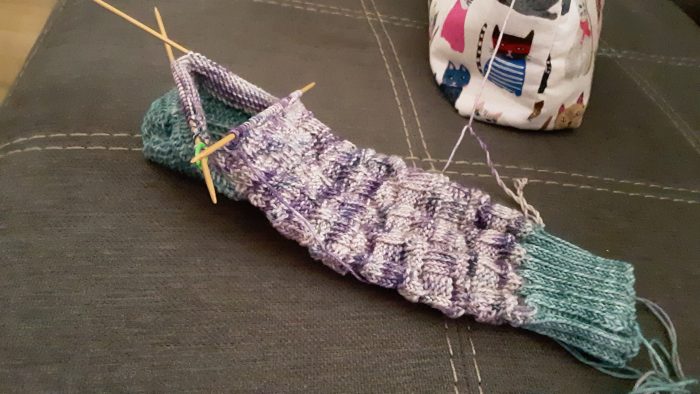a half-knitted sock in purple and green variegated yarn
