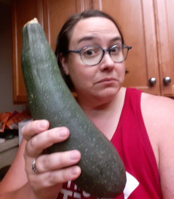 me with a startled expression, holding a large zucchini