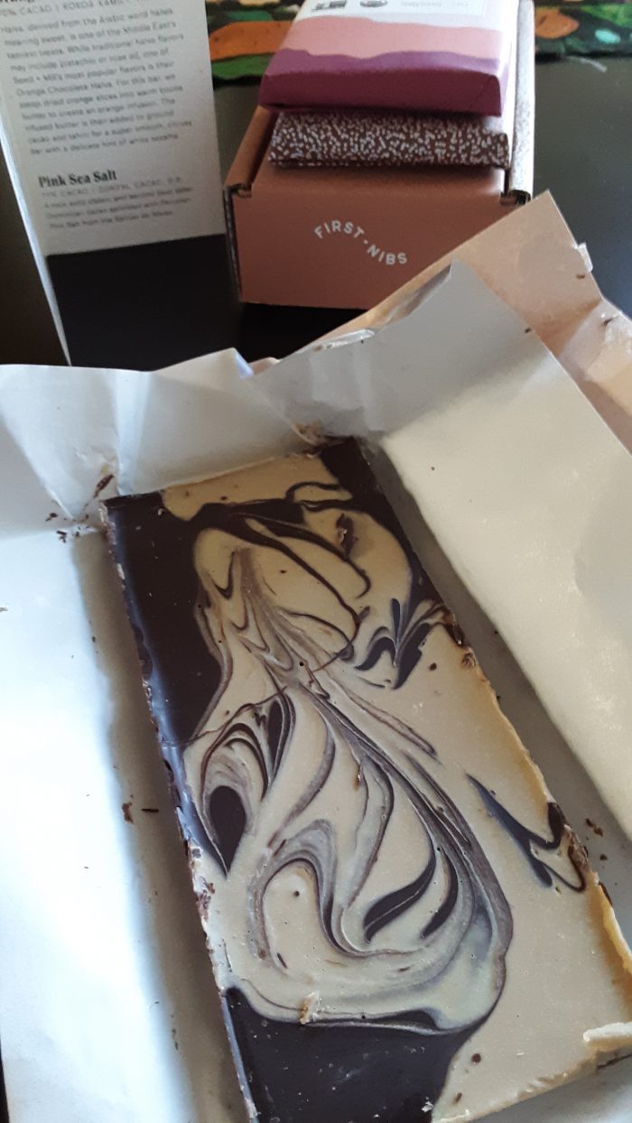 a bar of chocolate situated in an open wrapper plus two wrapped bars in the background