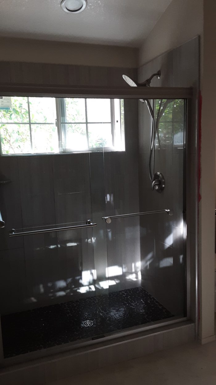 shower with glass door, large grey tiles, and black "pebble" floor