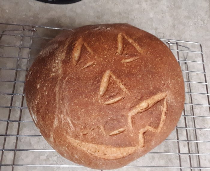 a round loaf of rye bread scored with a jack-o-lantern style face