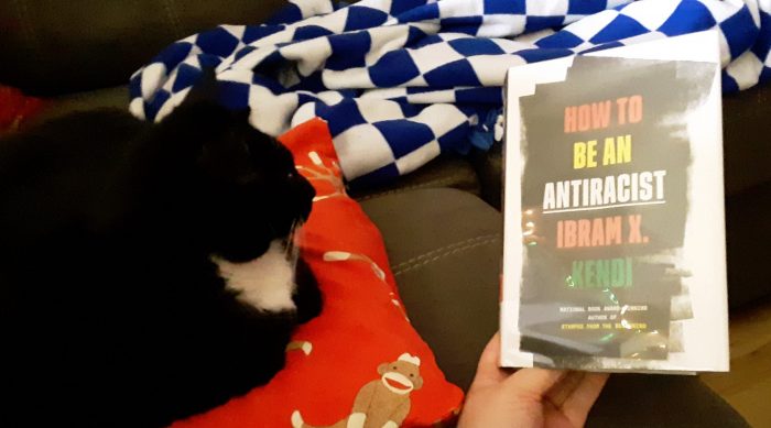 Huey the black cat next to the book How to Be an Anti-Racist