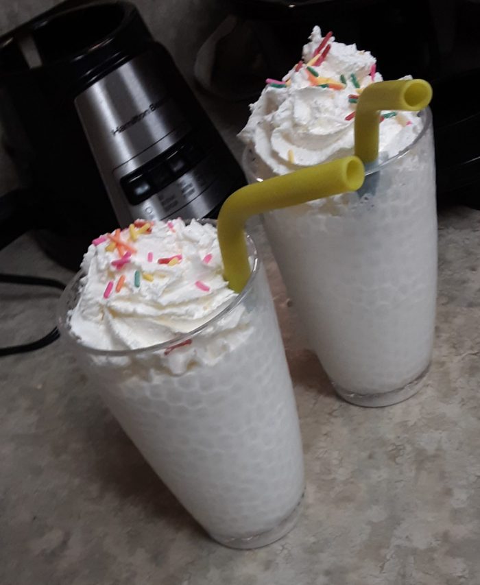 two milkshakes topped with whipped cream and sprinkles