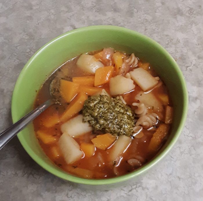 a bowl of winter minestrone soup topped with pesto