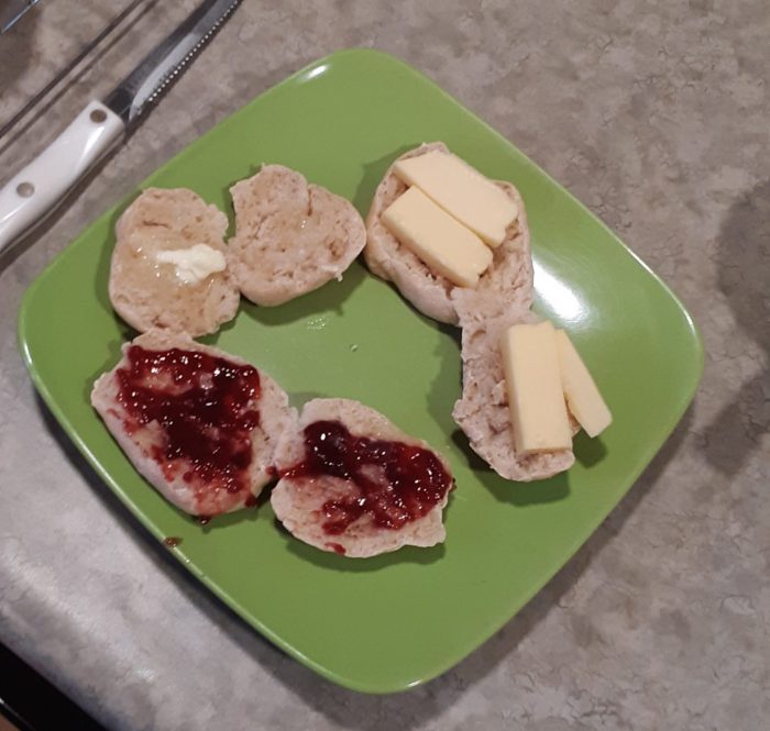 breakfast buns split in half on a plate, topped with butter, jam, and cheese respectively
