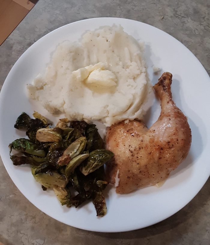 a plate with mashed potatoes, brussels sprouts, and a chicken thigh and drumstick