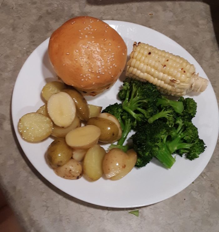a plate with a cheeseburger, broccoli, fingerling potatoes and corn on the cob