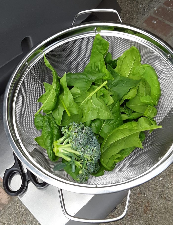 a mesh strainer containing spinach and a small broccoli crown