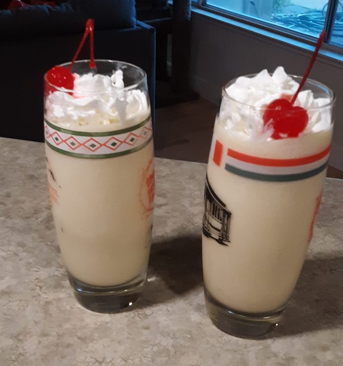 two glasses of alcohol-free piña coladas adorned with whipped cream and a cherry