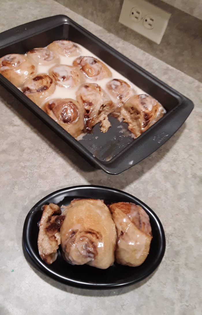 a pan of sourdough cinnamon rolls next two a plate with two rolls