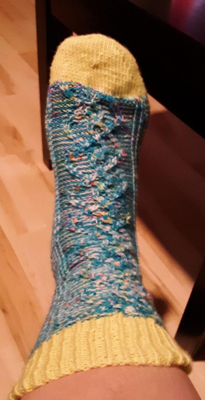 finished sock on my foot. The sock is made of a varigated blue yarn and has a cable pattern