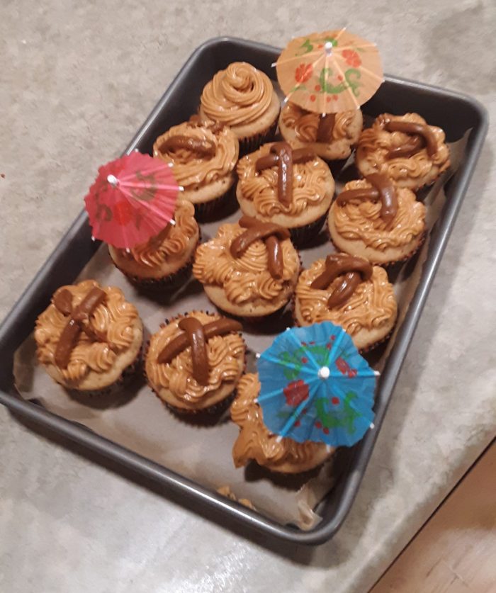 12 dulce de leche cupcakes in a pan. paper/toothpick umbrellas are stuck into three cupcakes