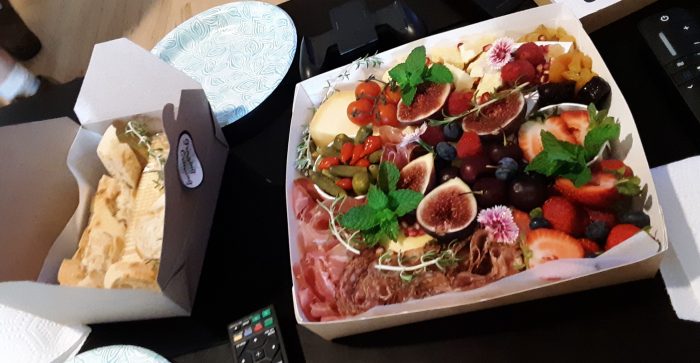 a large box of charcuterie topped with lots of fruit, plus a smaller box of bread and crackers