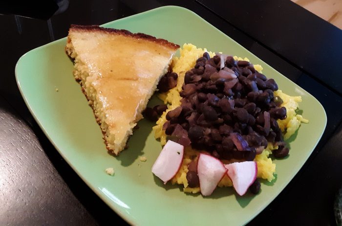 a plat with a pile of beans and rice next to a slice of cornbread