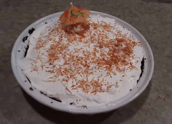 top view of a coconut cream pie, we mostly see a layer of whipped cream with toasted coconut on top