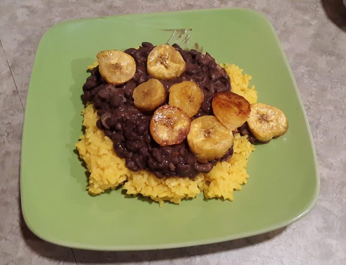 A plate of black beans and yellow rice with plaintains on top