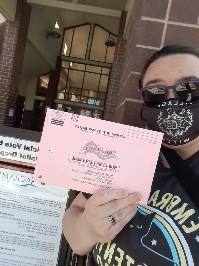 a selfie of me holding up my ballot in front of the ballot drop box at the library