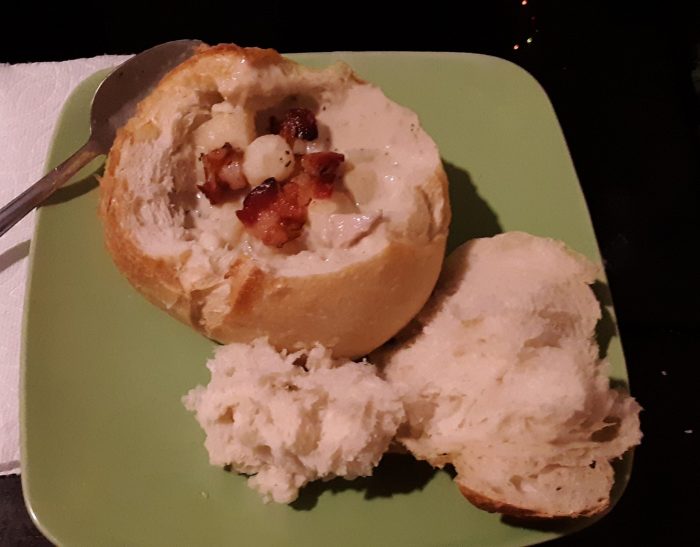 a bread bowl containing clam chowder, on a green plate
