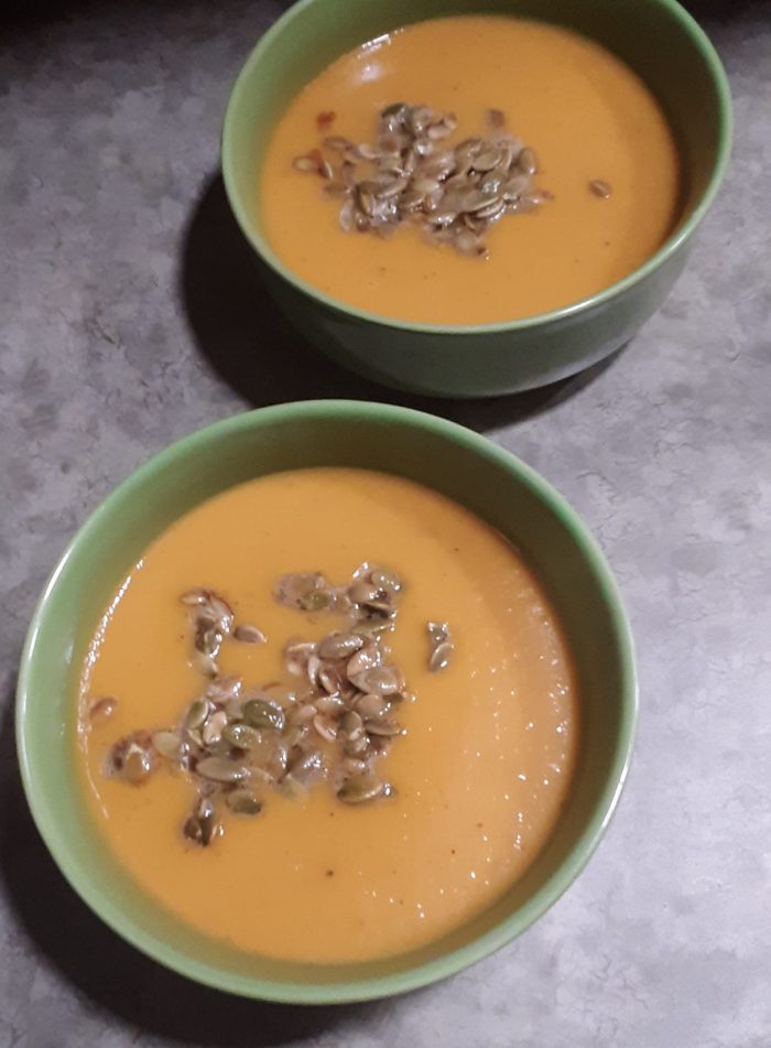 two bowls of butternut squash soup topped with pumpkin seeds