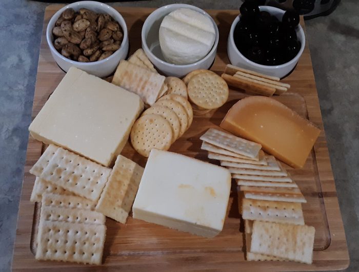 a wooden board covered with several types of cheese and crackers plus almonds and olives