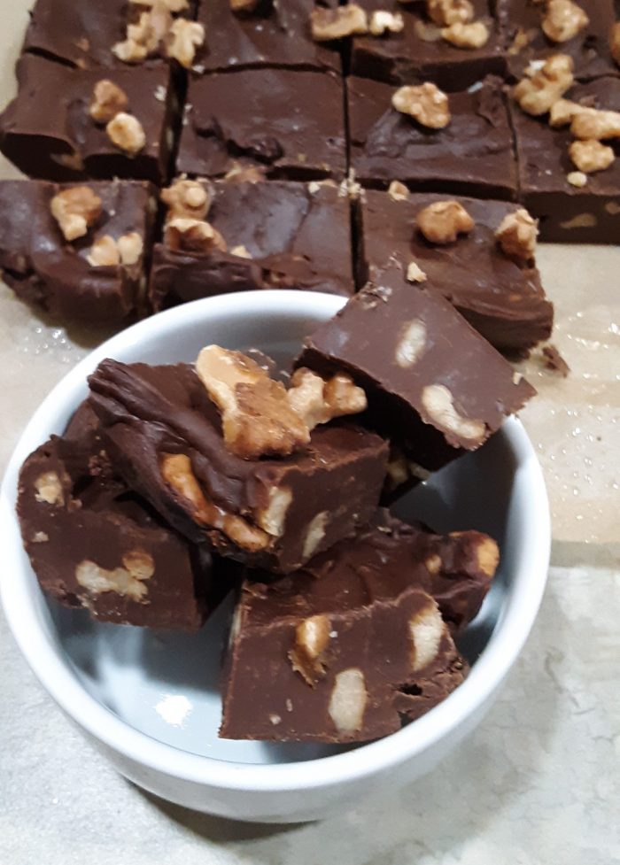 a small bowl with pieces of walnut fudge stacked in it and the rest of a block of fudge in the background