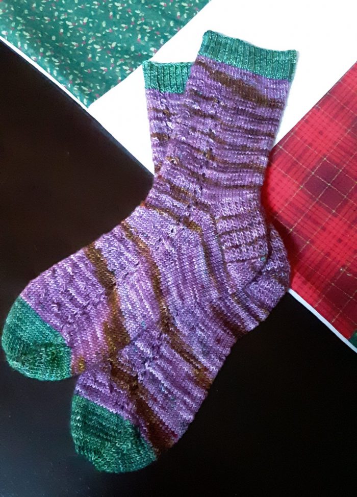 newly knit pair of socks. purple yarn with green cuff and toe