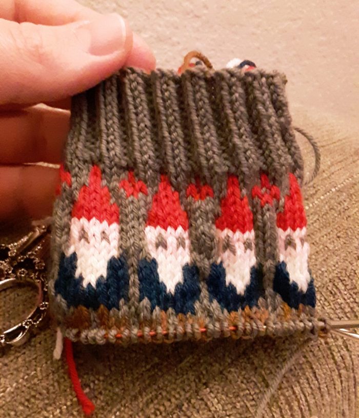 the beginning of a knit sock, including cuff and one round of a pattern of gnomes wearing pointy hats