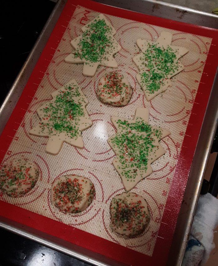 a pan of sugar cookies, some in balls and some cut into christmas tree shapes, covered with festive sprinkes