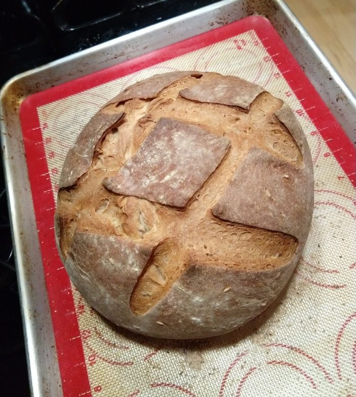 a round of freshly baked rye bread on the baking sheet. It is scored with a cross-hatched pattern