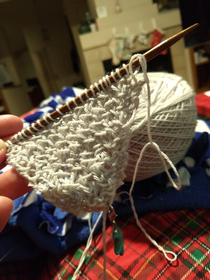 a small triangle of knitting hanging on the needle. Christmas stockings are in the background