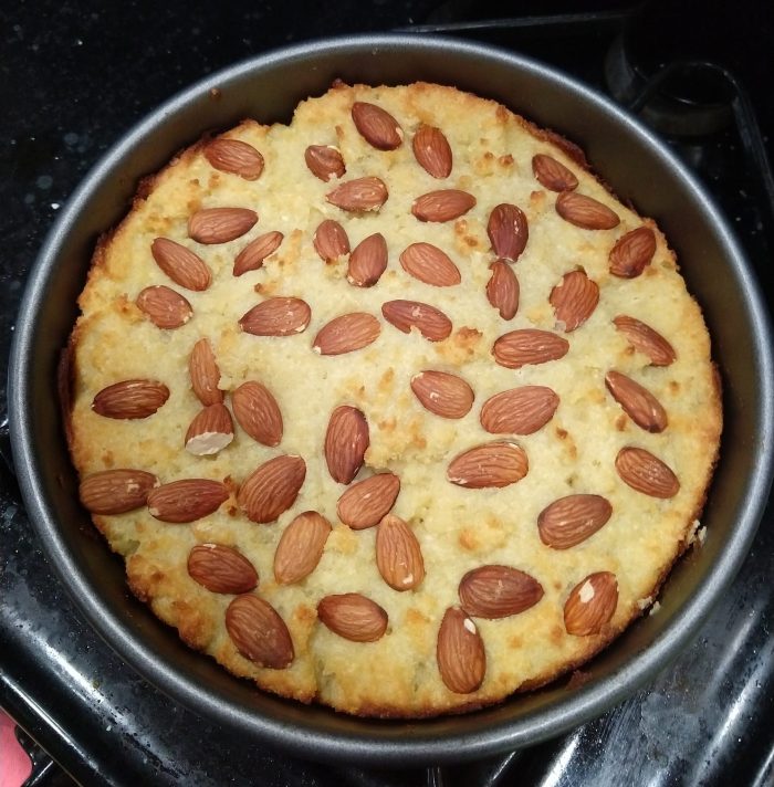 a semolina cake topped with whole almonds, in an 8-inch cake pan