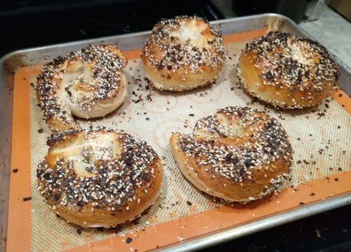 five everything bagels on a baking sheet that has just been removed from the oven
