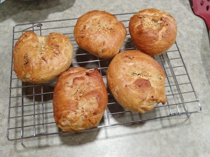 five bagels cooling on a wire rack. the bagels are topped with minced onion