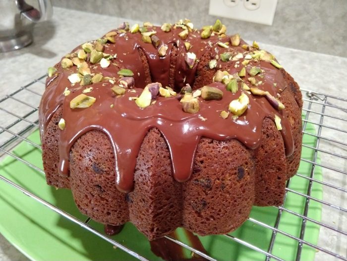a chocolate pistachio bundt cake dripping with chocolate ganache and topped with chopped pistachios