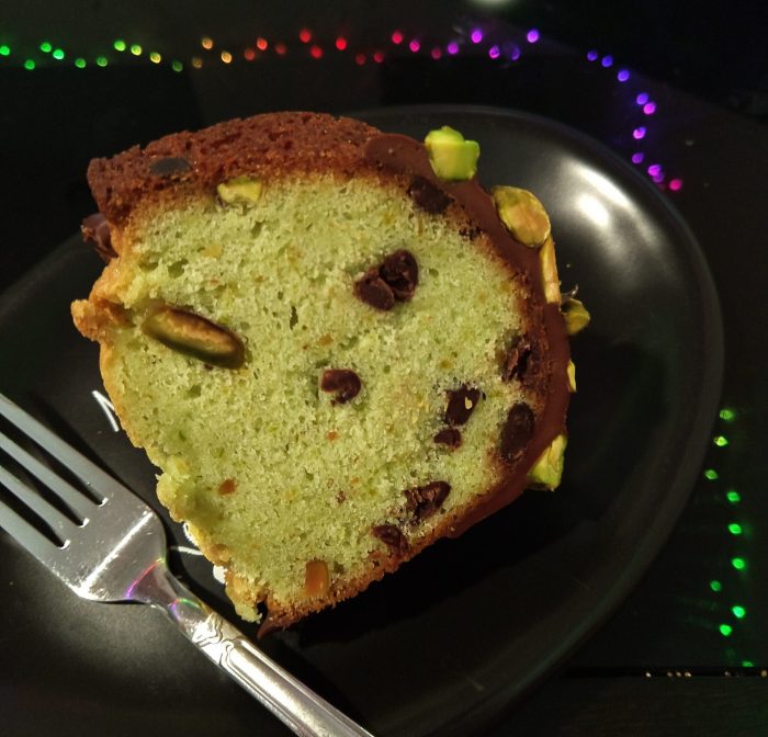 a slice of chocolate pistachio bundt cake, revealing a light green interior studded with chocolate ships and pistachios