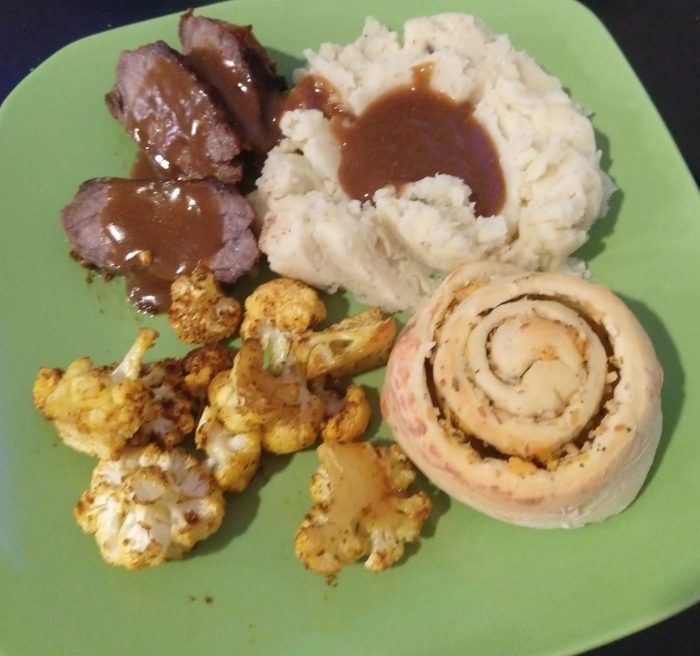 a plate with tri tip, mashed potatoes, spiced cauliflower, and a cheesy onion roll