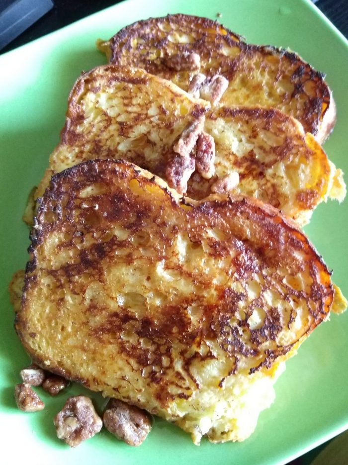 a plate of three slices of brioche french toast topped with syrup and pecans