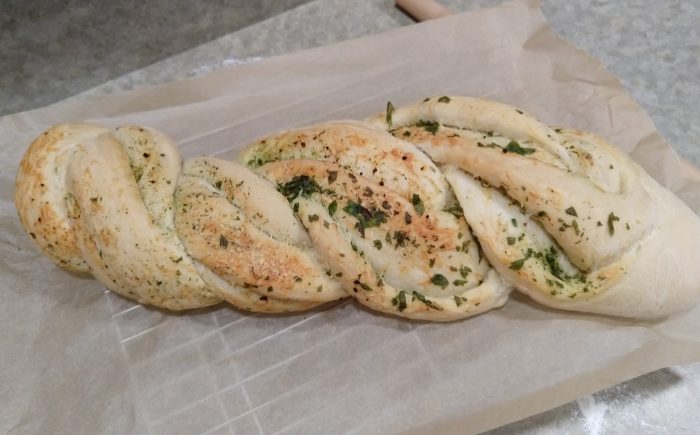 a loaf of bread that has strands twisted around to reveal cheese and herbs inside