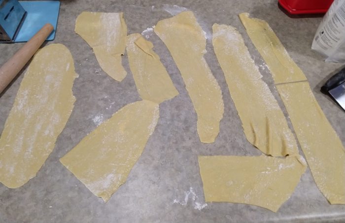 somewhat irregularly shaped sheets of pasta laid out on the counter in preparation for cooking