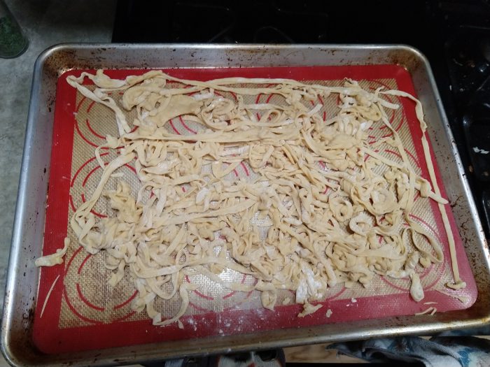 a sheet pan of uncooked fettuchini noodles. The noodles are tangled, stuck together, and uneven.