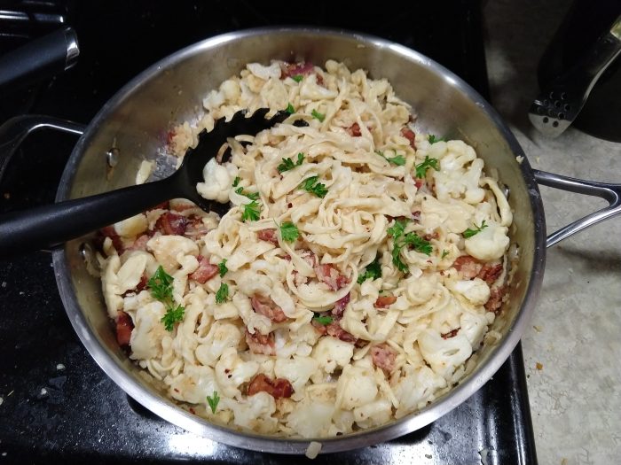 a large skilled of hommade pasta mixed with small pieces of bacon and cauliflower florettes