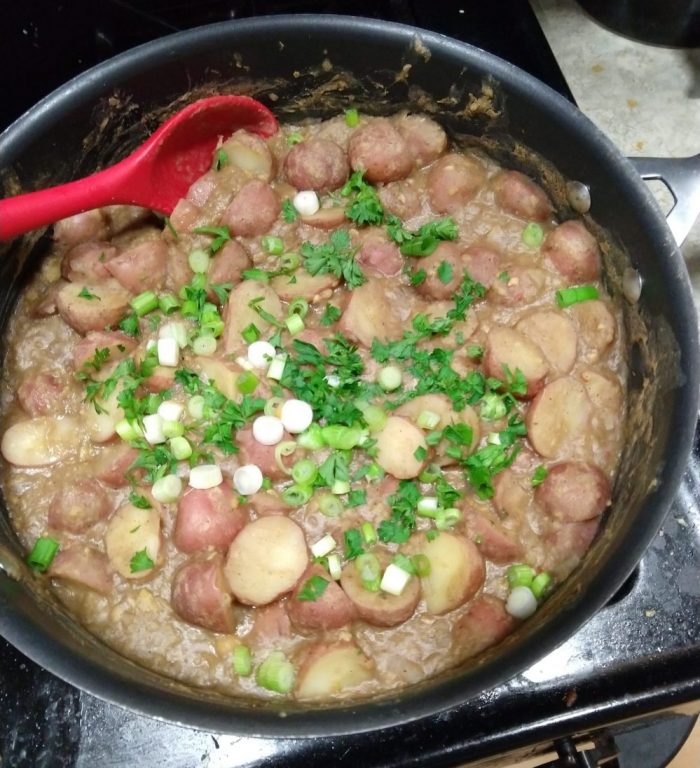 a skillet of braised potatoes and chickpeas, topped with bits of green onion and parsley