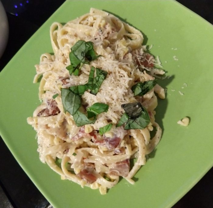 a plate of creamy pasta studded with corn and bacon, topped with basil and parmesan
