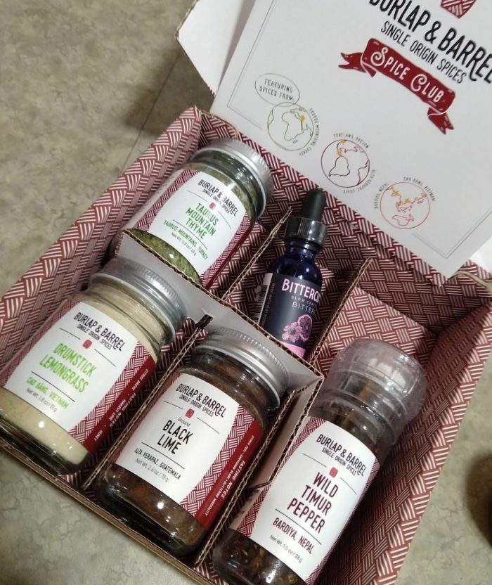 Burlap and Barrel spice club shipment. Spices are arranged in a small box with dividers. Included are: jars of taurus mountain thyme, drumstick lemongrass, black lime, a grinder of wild timur pepper and a dropper of biters.