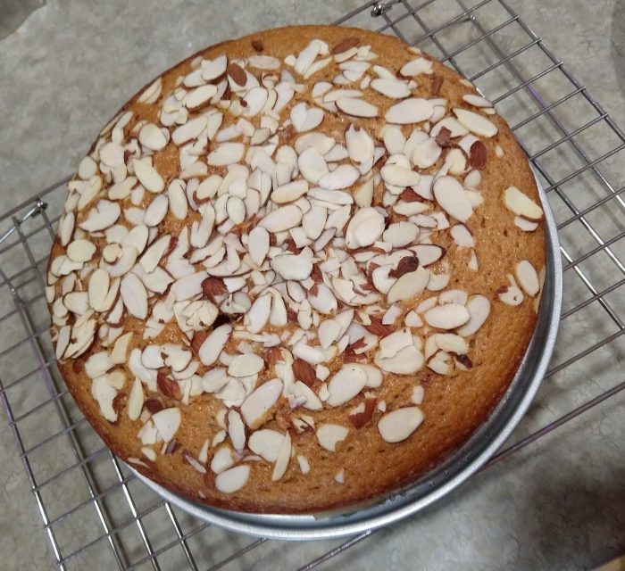 a 9-inch round cake, golden brown, covered in sliced almonds, cooling on a wire rack