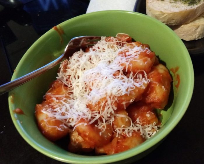 a bowl of homemade potato gnocchi in a tomato sauce, topped with shredded cheese