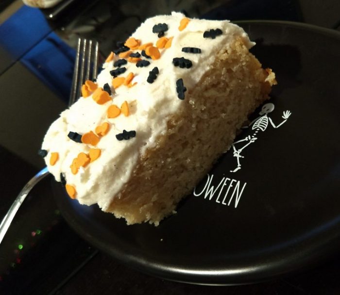 a square piece of vanilla cake topped with buttercream frosting and halloween sprinkles on a small plate