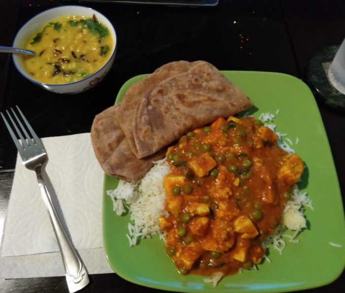 a plat of matar paneer (peas and cheese in tomato sauce), rice, and paratha (layered flatbread), plus a small bowl of lentils
