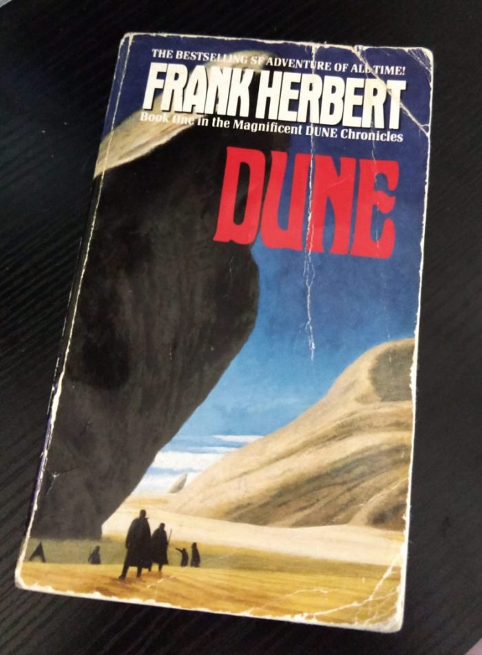 a worn paperback copy of Dune showing a large rock outcropping and silhouettes of people walking in the desert